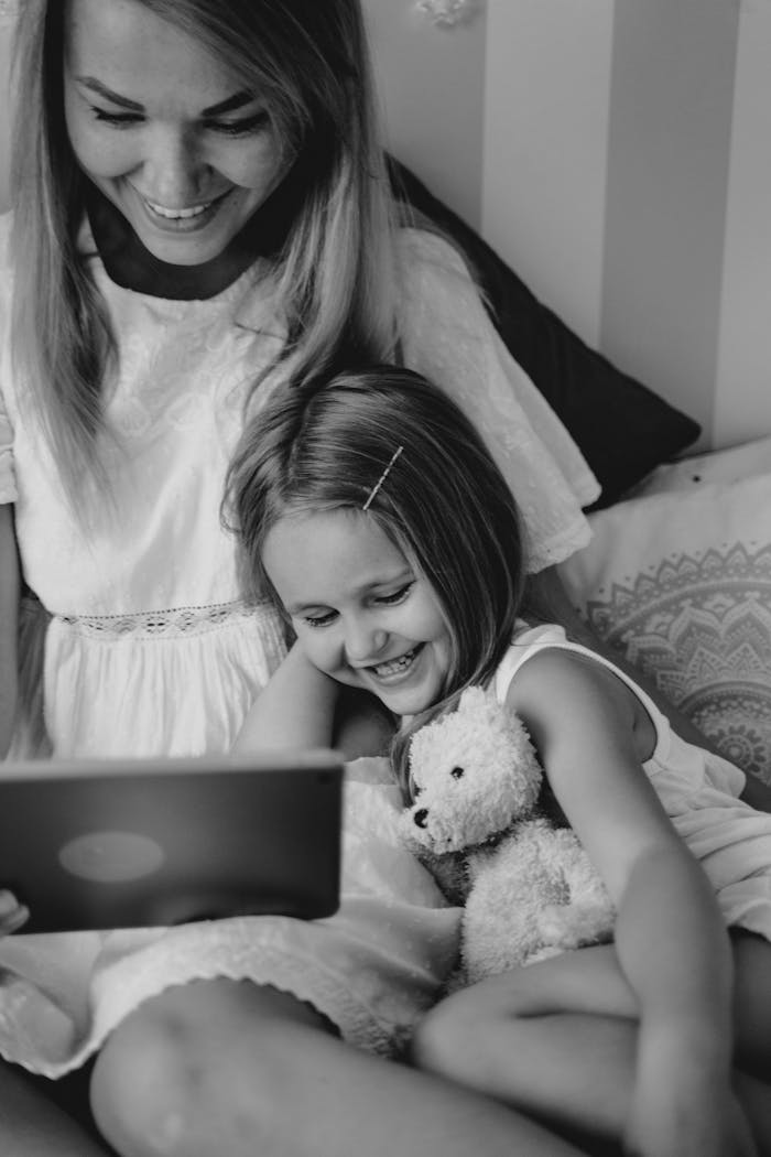 Mother and daughter bonding over a tablet, sharing joyful moments indoors.