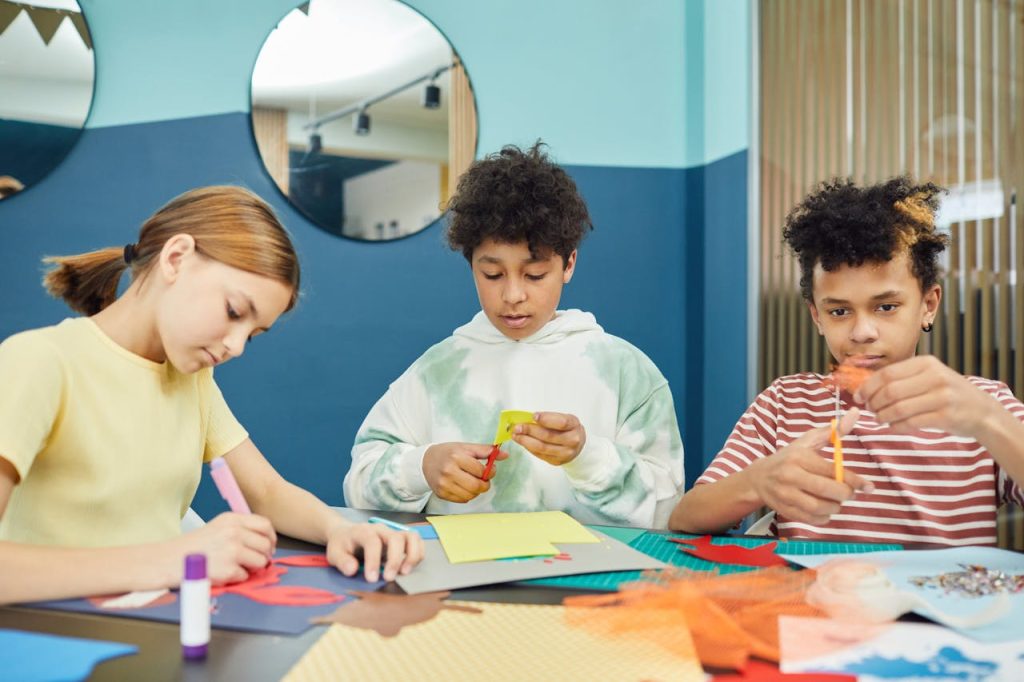 multiethnic-kids-making-drawings-in-art-school-7869446 Group of concentrated multiracial children making artworks with colorful paper and scissors while sitting at table in light room